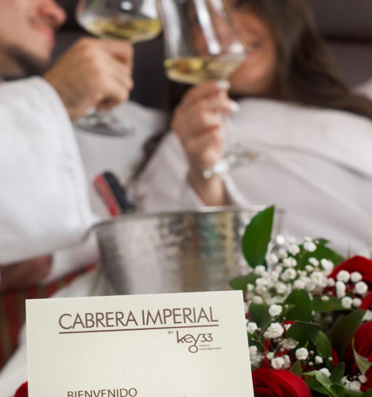 Mesa con pareja brindando y vino; tarjeta &ldquo;Cabrera Imperial&rdquo; en primer plano.