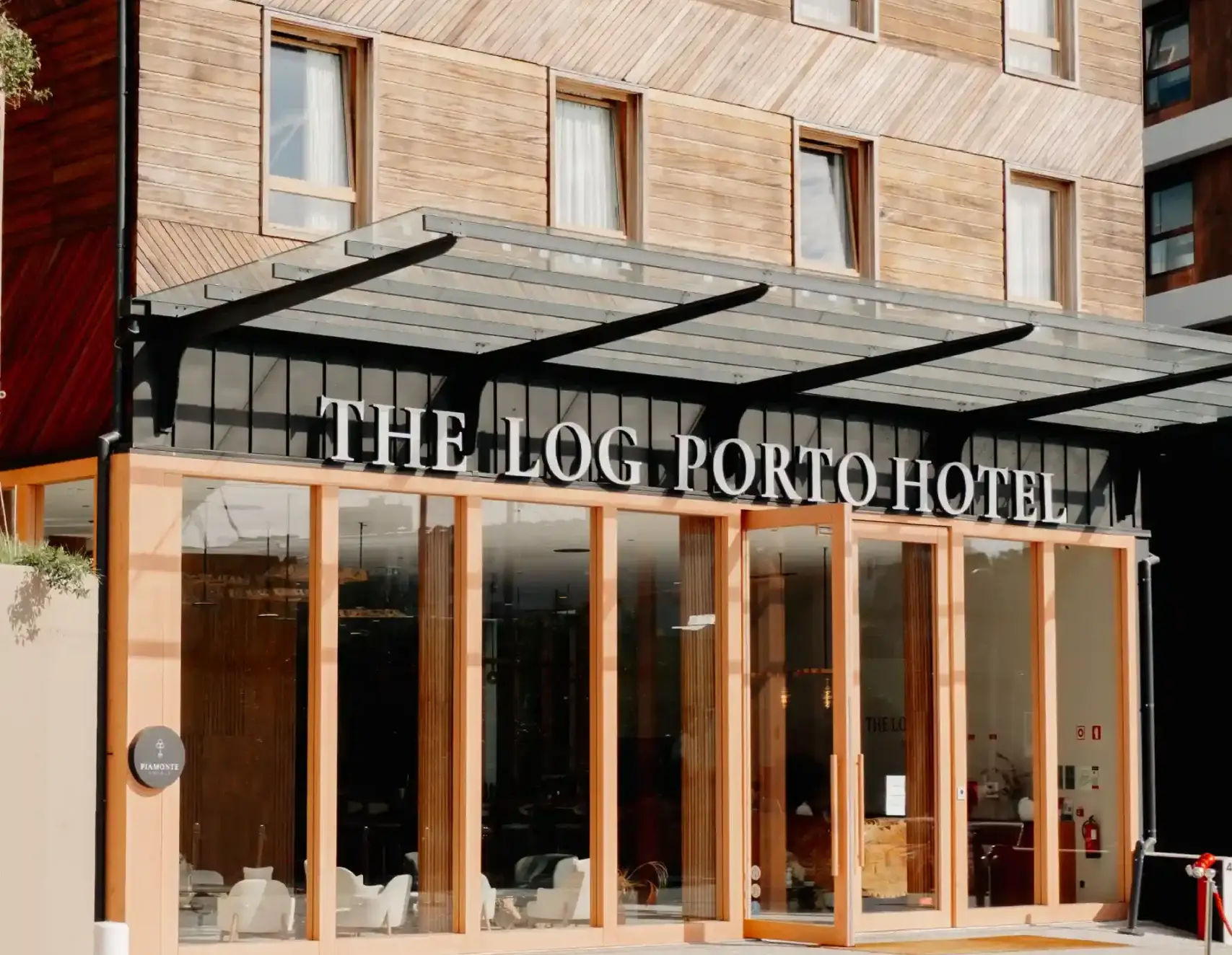 Entrada elegante do The Log Porto Hotel com fachada de madeira e vidro.