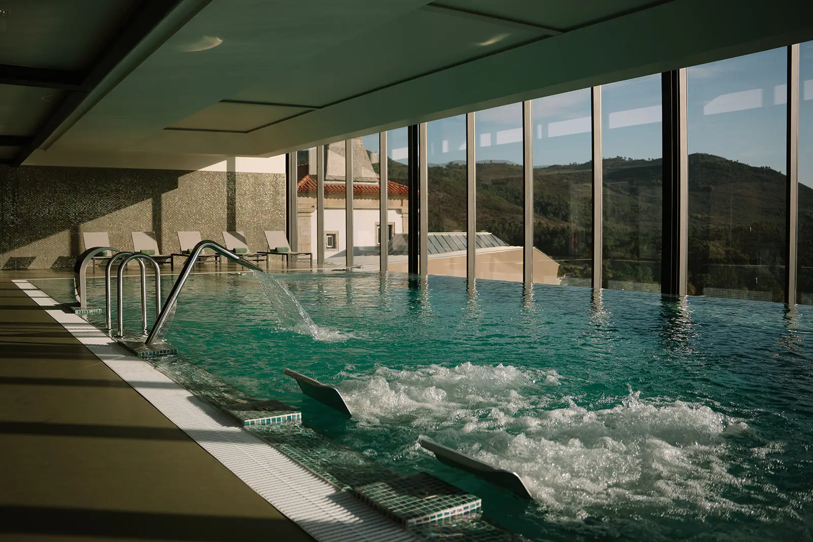 Piscina interna com vista para montanhas atrav&eacute;s de janelas.