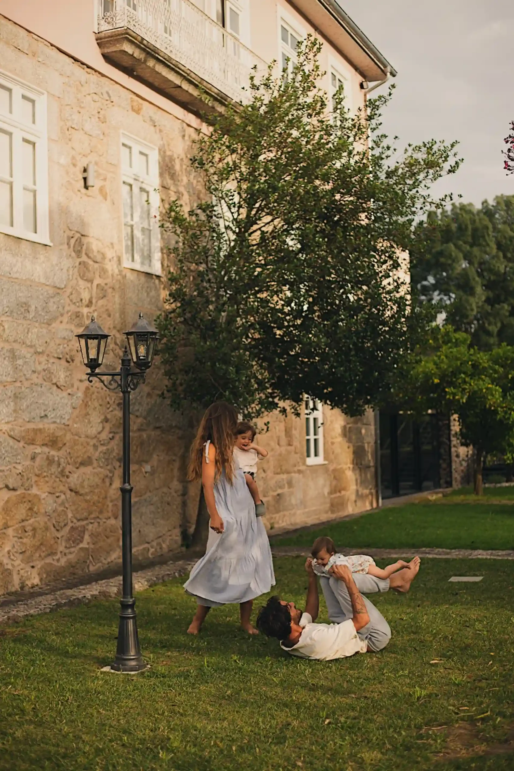 Crian&ccedil;as brincando com um adulto no jardim ao lado de uma casa de pedra.