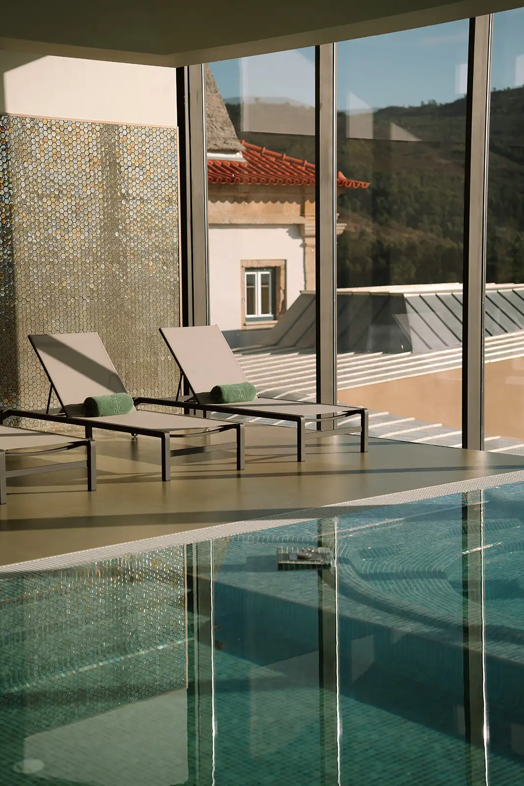 Espregui&ccedil;adeiras e piscina interna com vista para telhados e colina ao fundo.
