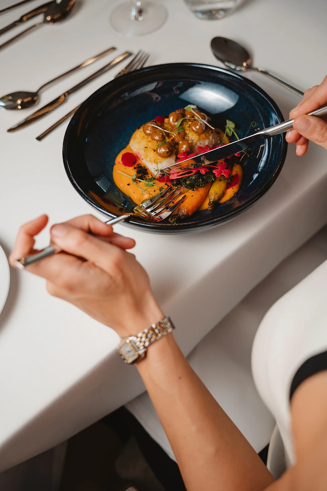 Pessoa cortando prato gourmet em um restaurante elegante.