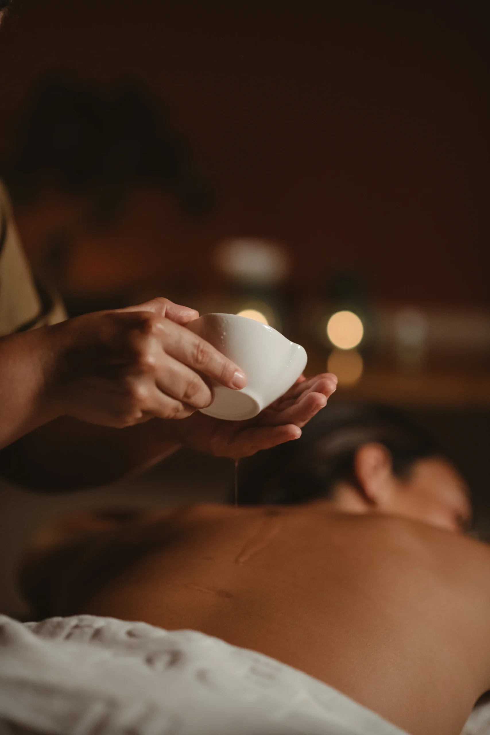 Pessoa recebendo &oacute;leo de massagem nas costas em ambiente relaxante.