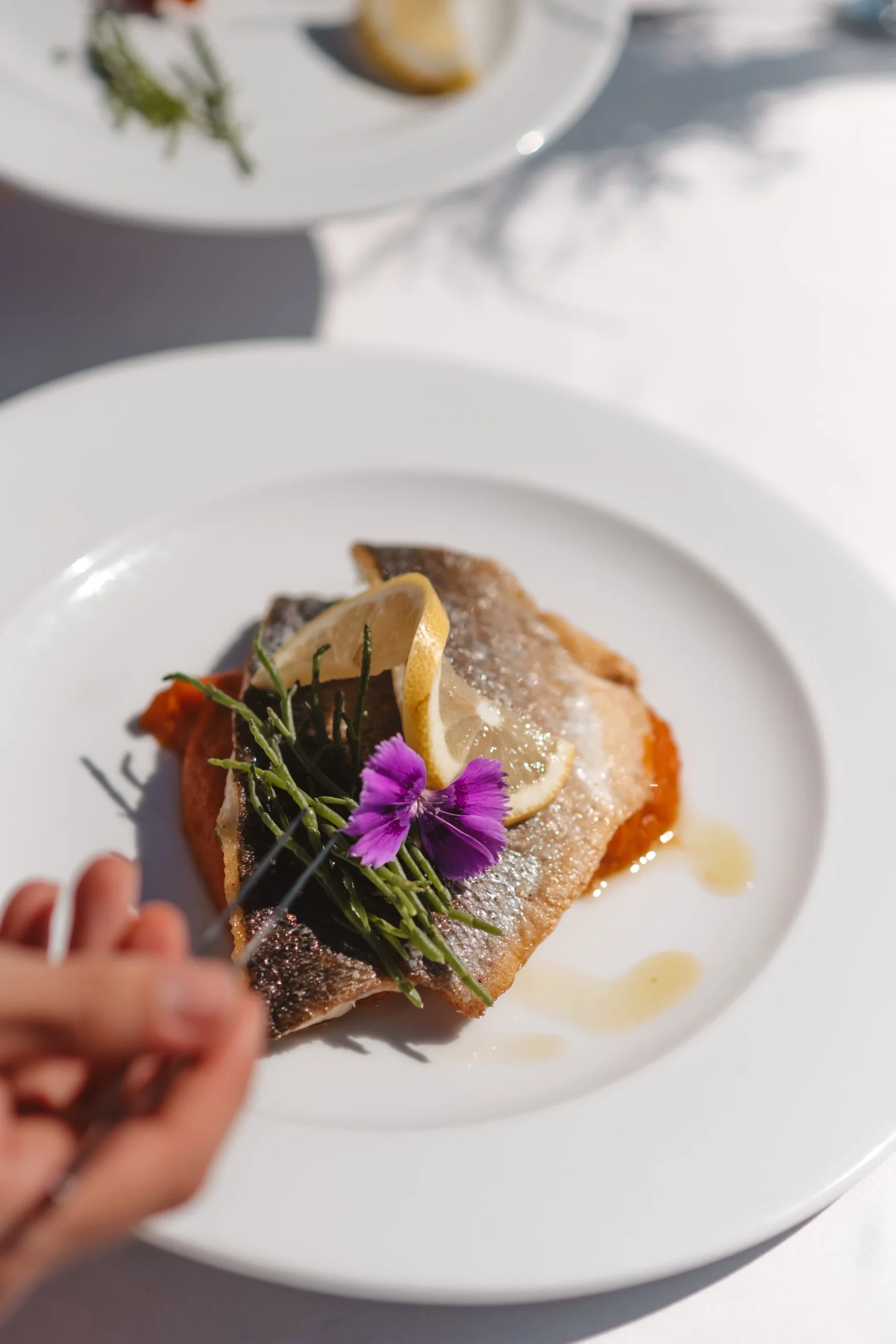 Prato de peixe com lim&atilde;o, flor roxa e ervas decorativas.