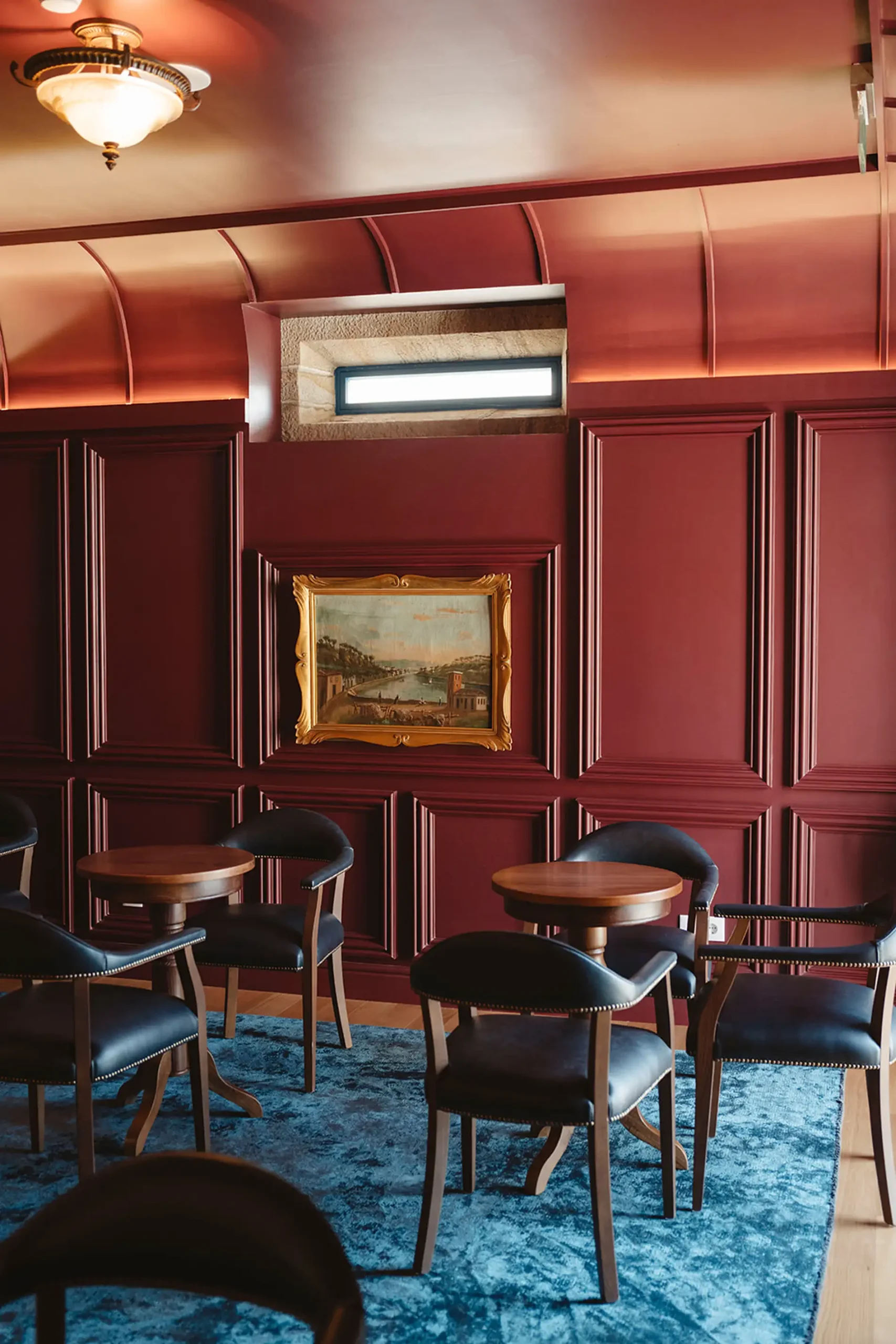 Sala com paredes vermelhas, mesas, cadeiras e tapete azul.