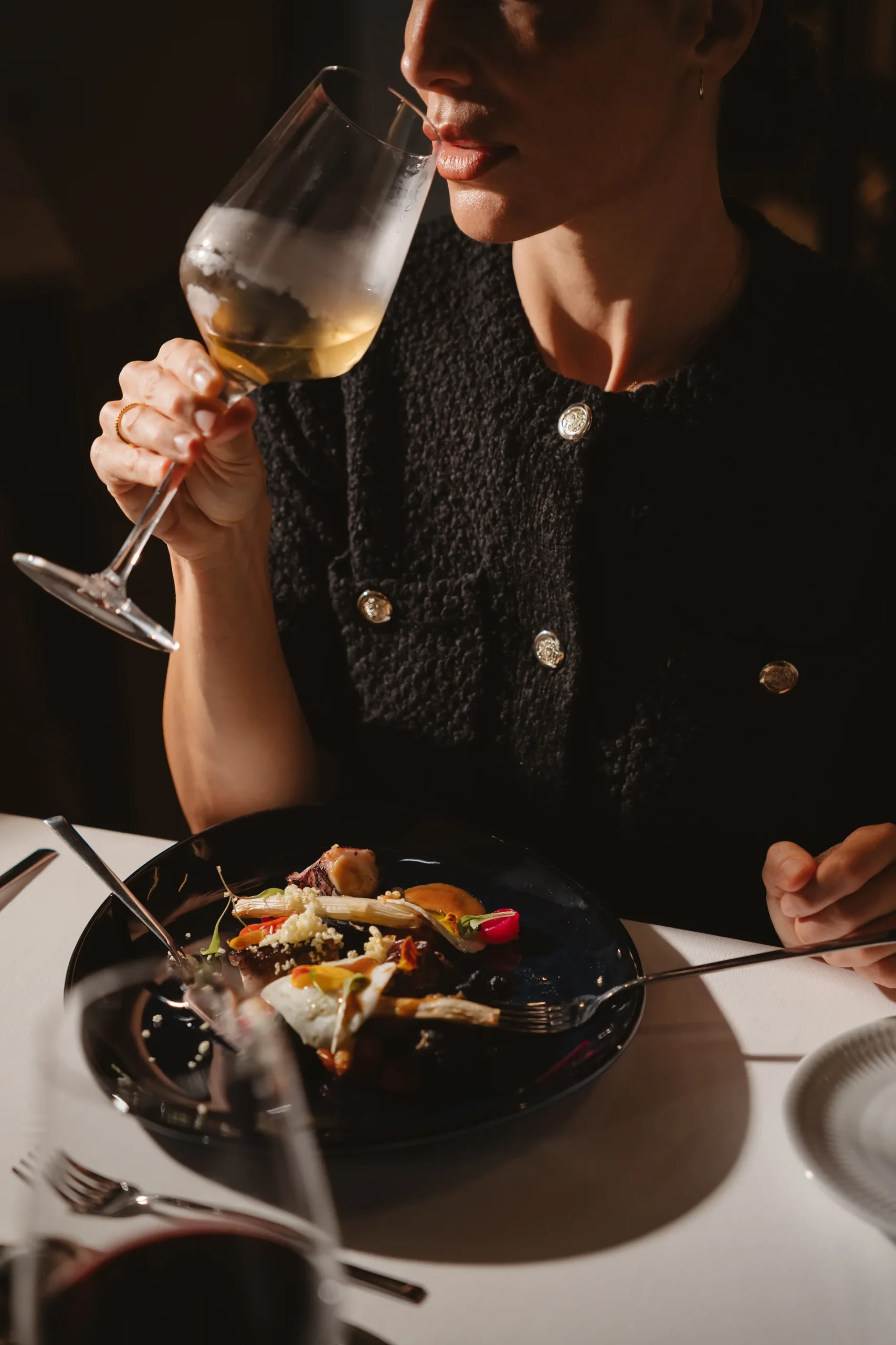Pessoa bebendo vinho e comendo em um restaurante elegante.
