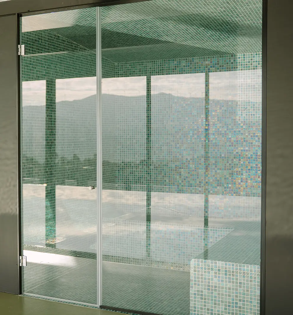 Porta de vidro com paredes revestidas em mosaico verde, vista do box