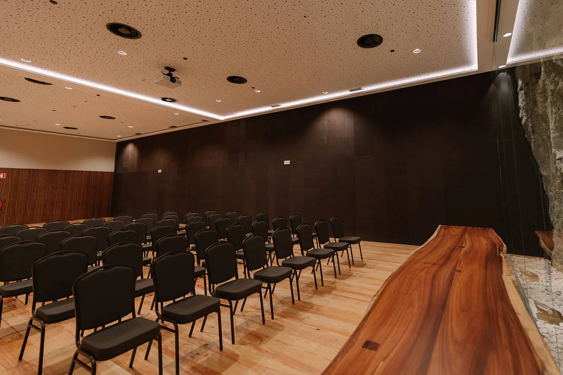 Sala de confer&ecirc;ncias vazia com cadeiras pretas e mesa de madeira.