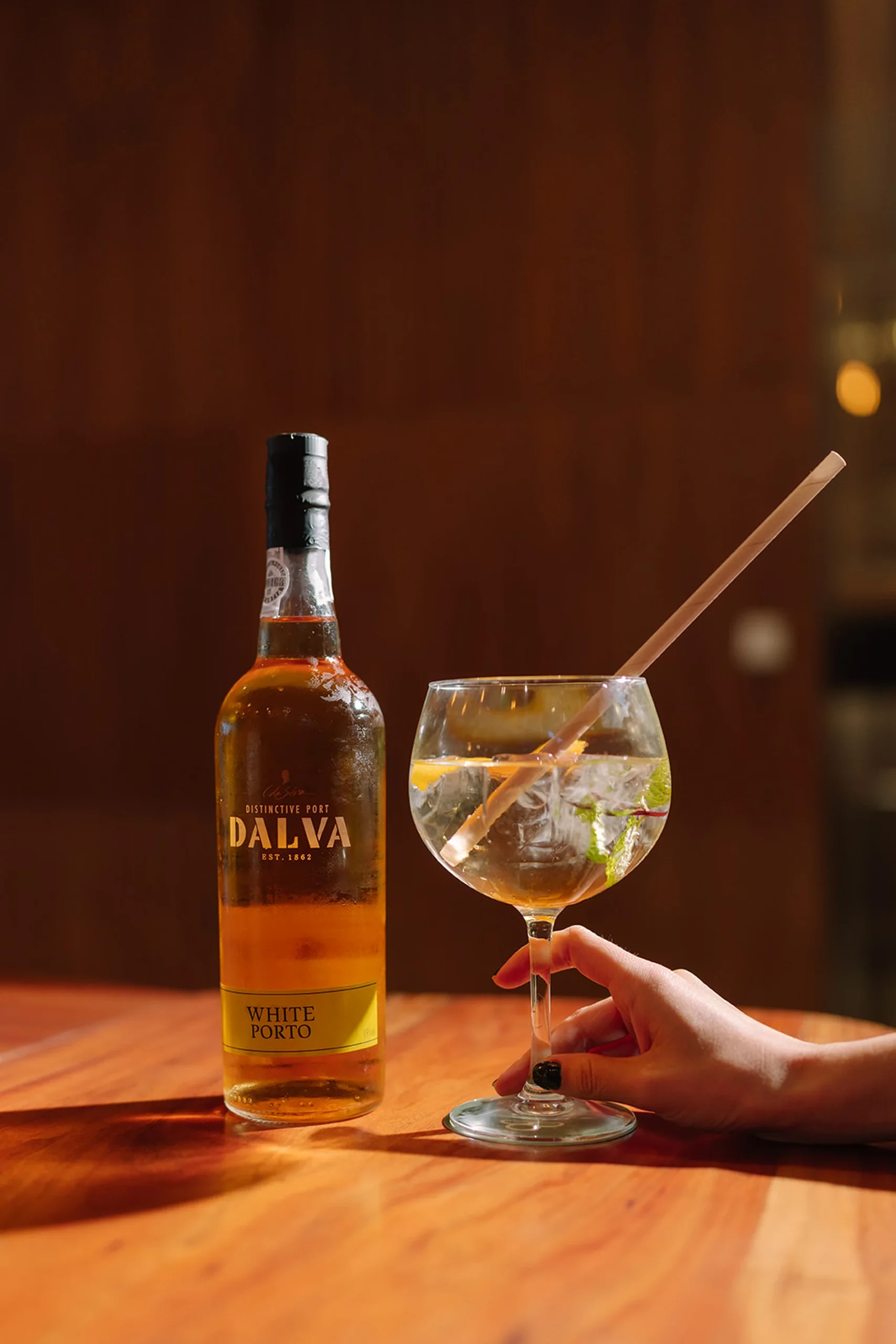 Garrafa de vinho do Porto e ta&ccedil;a com bebida, gelo e hortel&atilde; sobre a mesa.