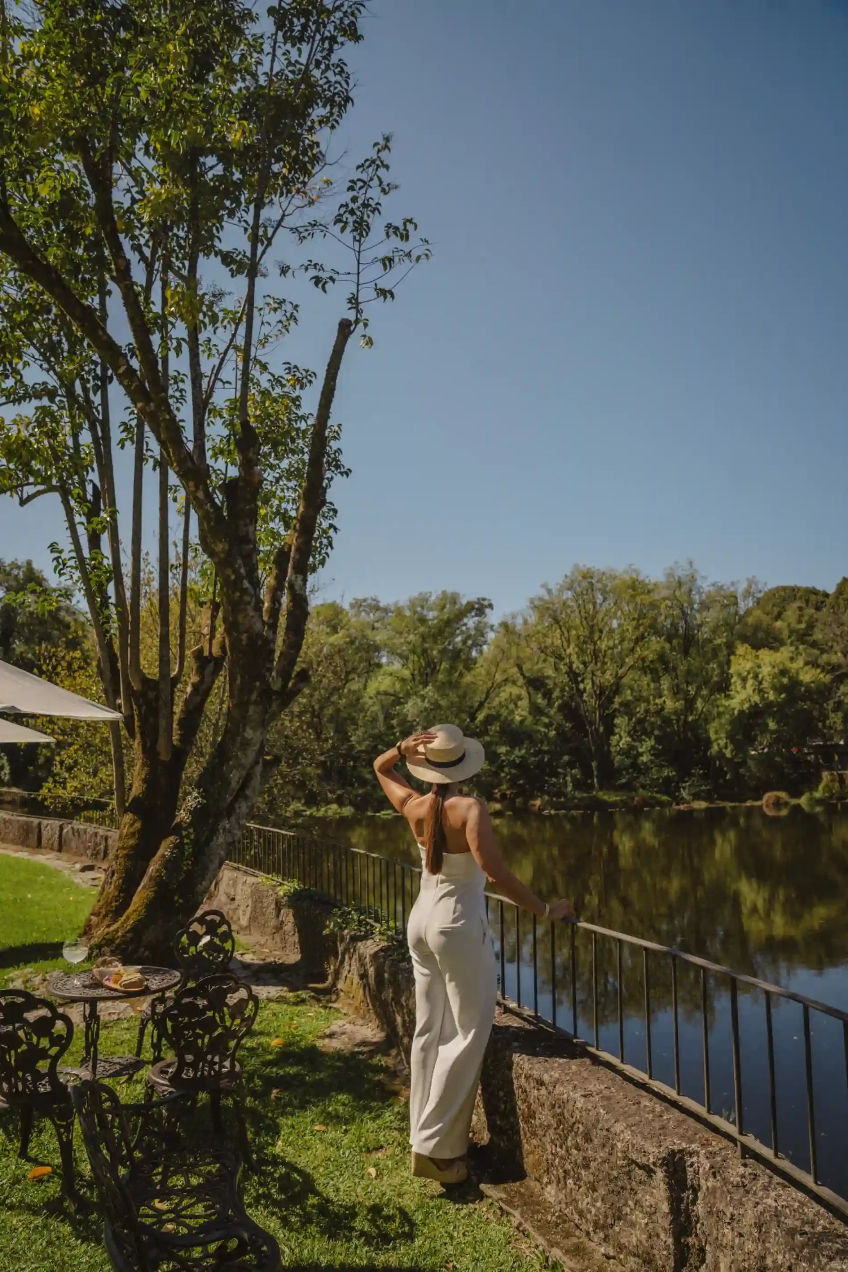 Mulher de chap&eacute;u posa ao ar livre em parque &agrave; beira de lago.