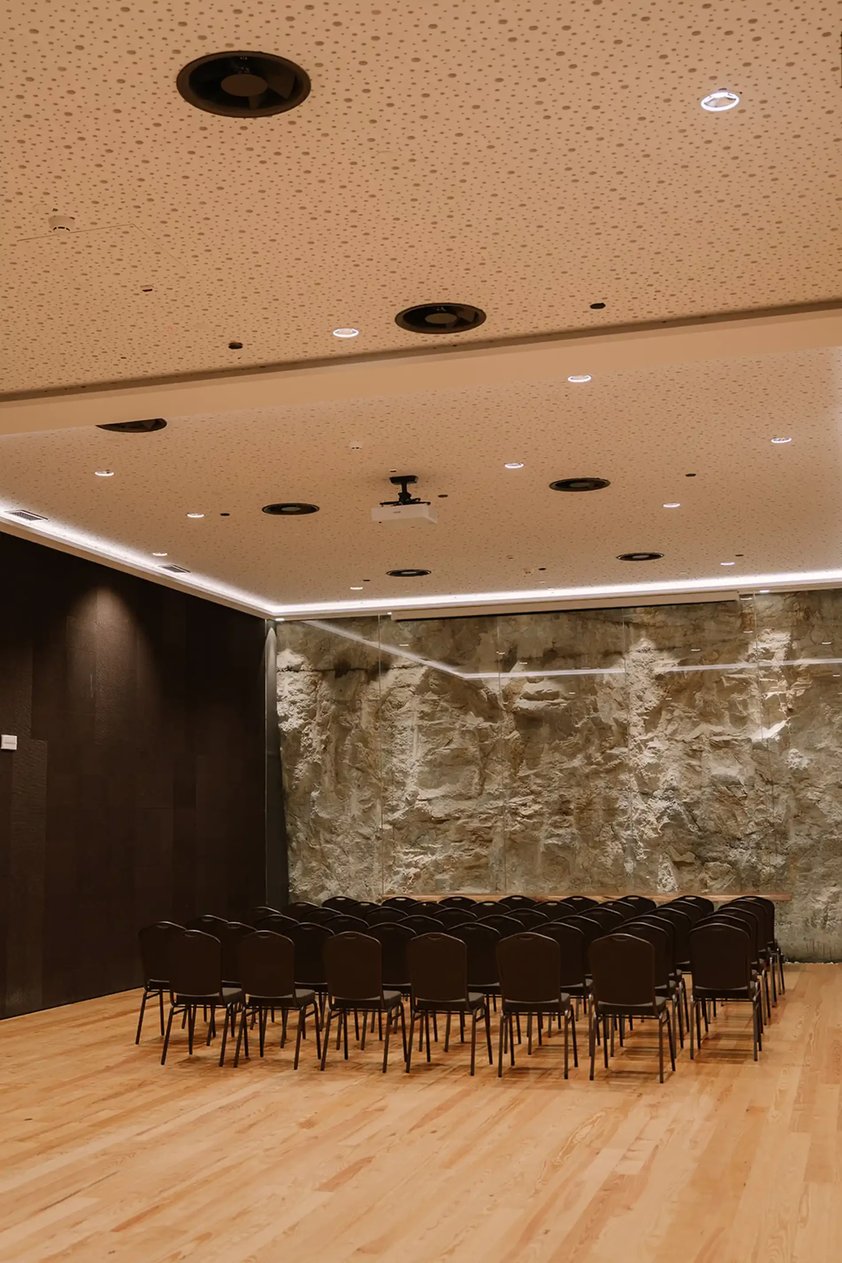 Audit&oacute;rio moderno com teto claro e parede de pedra ao fundo.