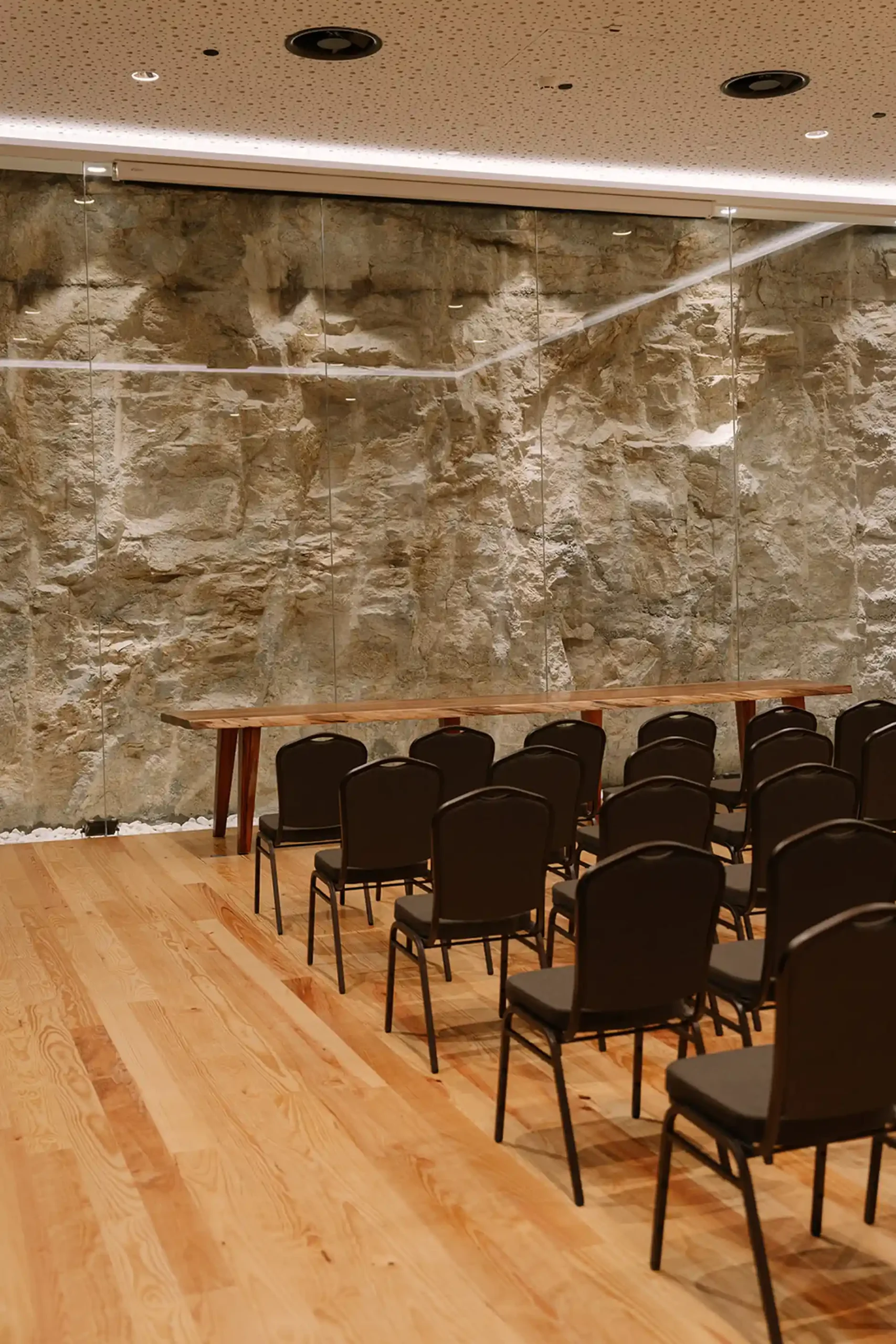 Sala de confer&ecirc;ncias com cadeiras e parede de pedra ao fundo.