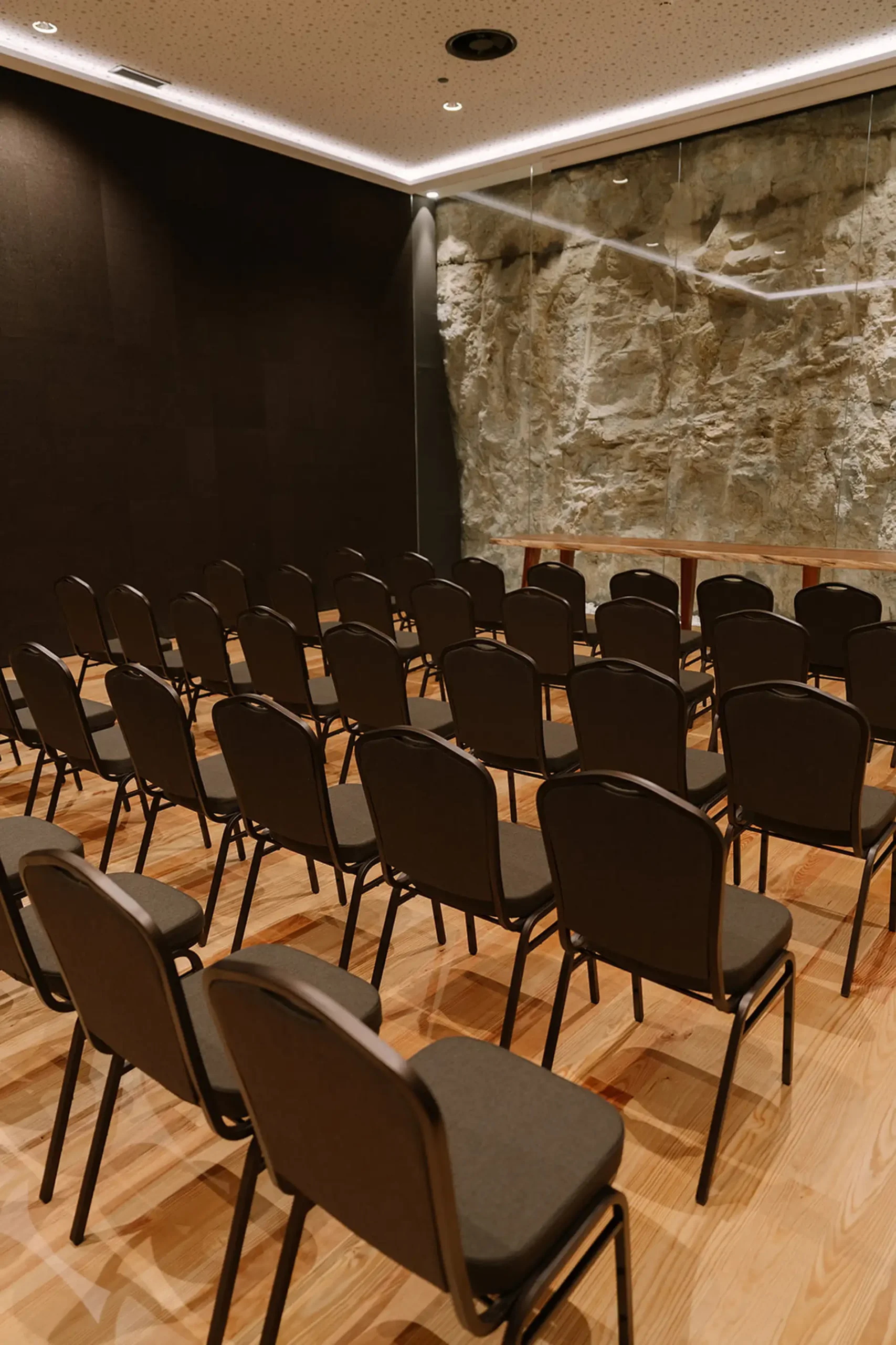 Sala de confer&ecirc;ncias com cadeiras vazias e parede de pedra.