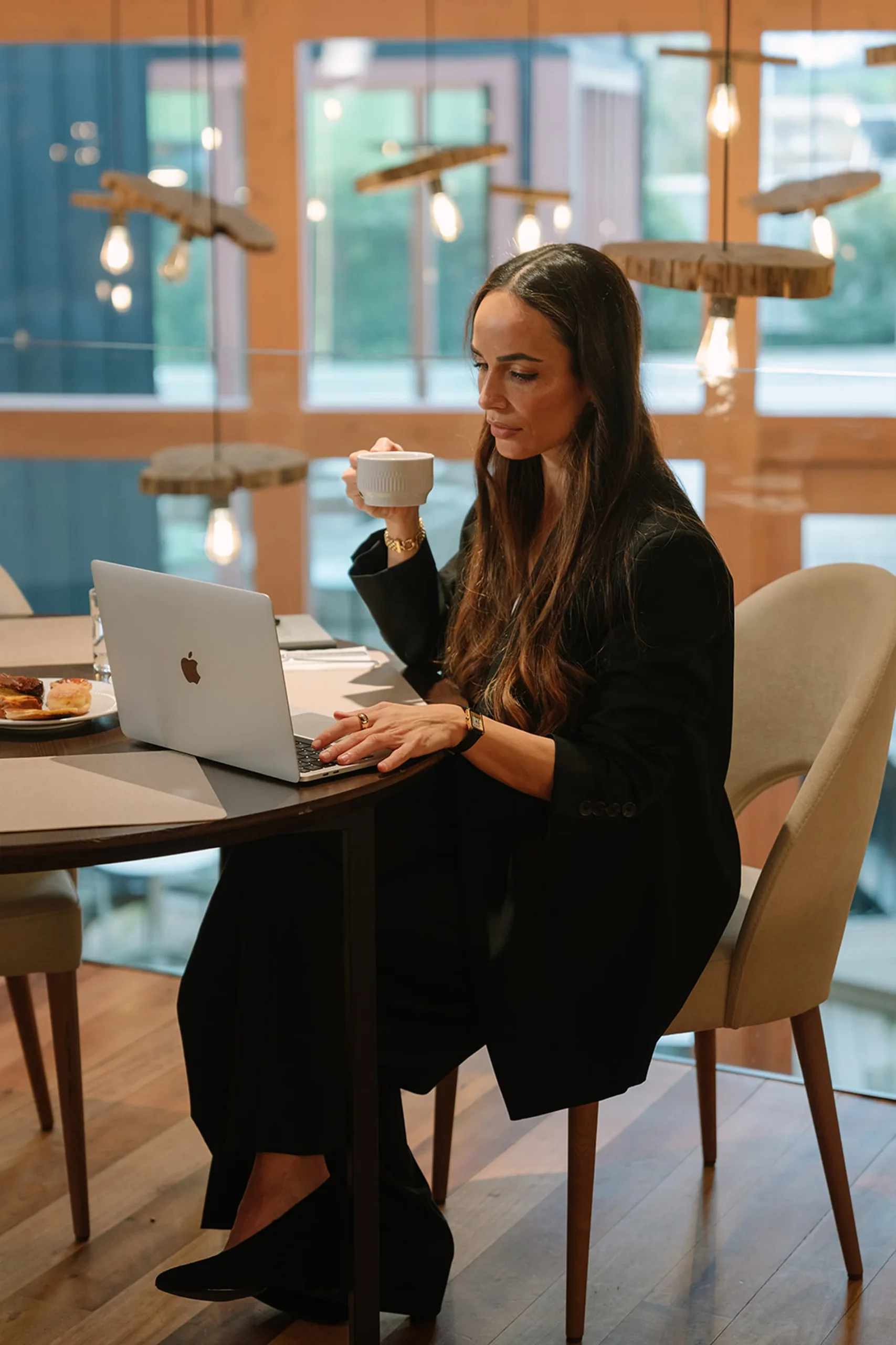 Mulher usando laptop e tomando caf&eacute; em uma cafeteria moderna.