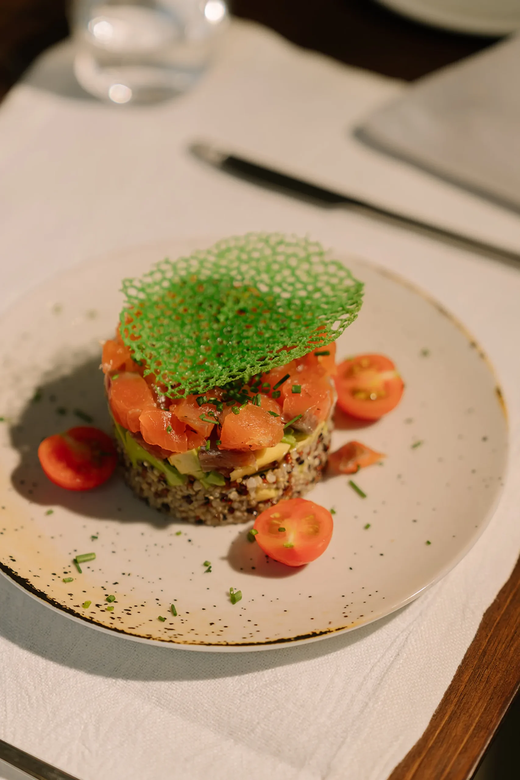 Prato com salm&atilde;o, abacate, gr&atilde;os e tomates, decorado com crocante verde.