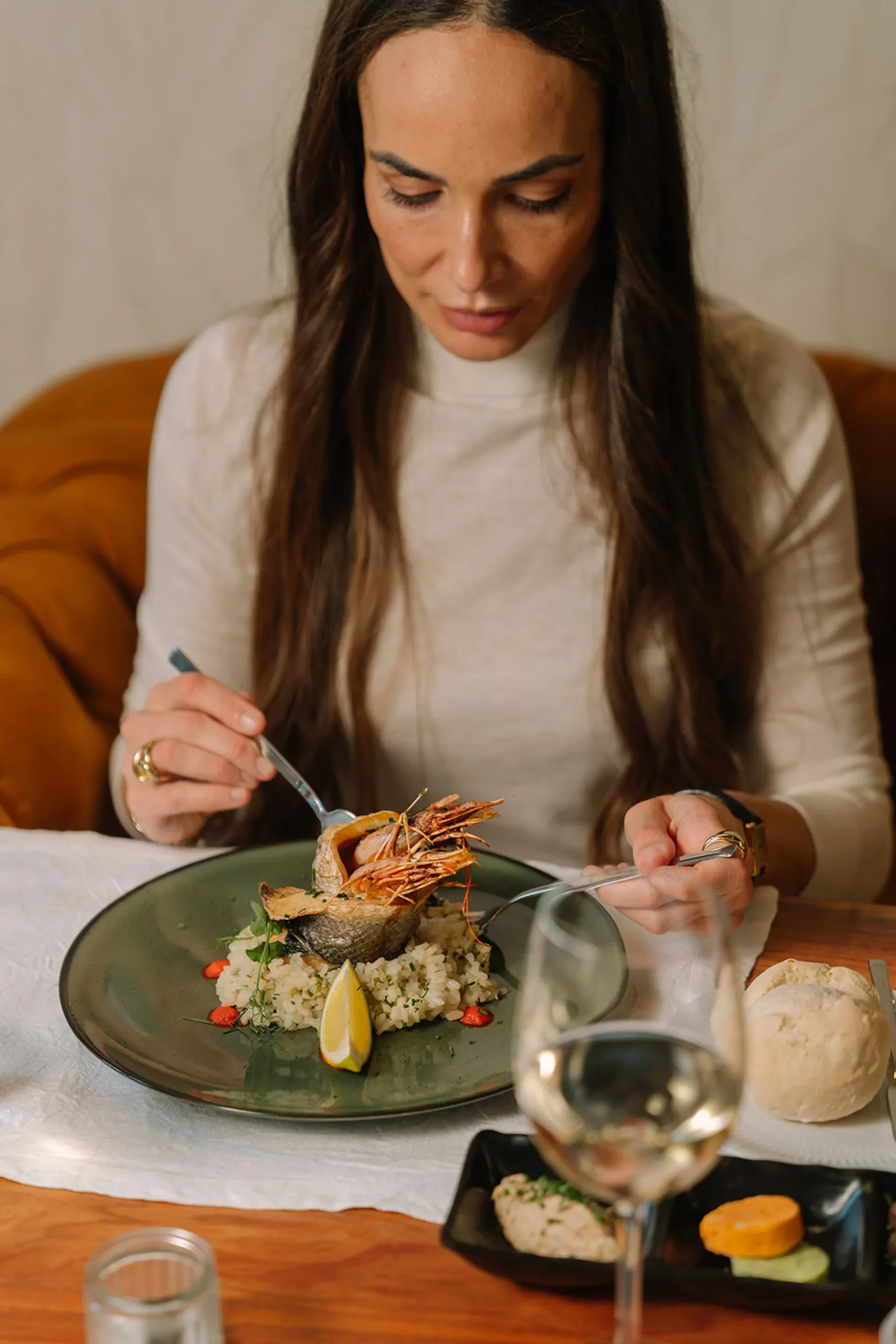 Mulher jantando prato gourmet com frutos do mar e arroz.