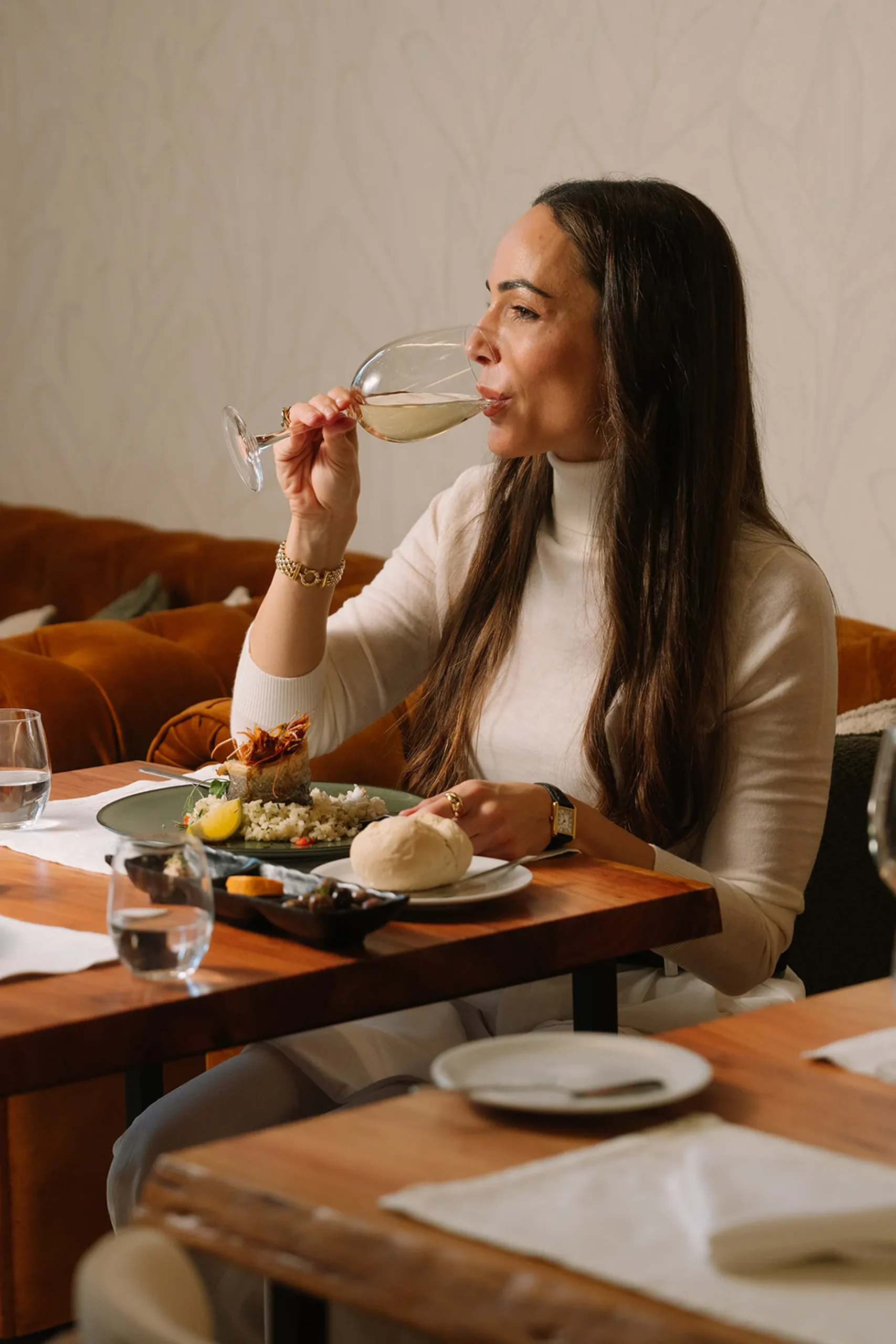 Mulher bebe vinho enquanto degusta uma refei&ccedil;&atilde;o em um restaurante elegante.