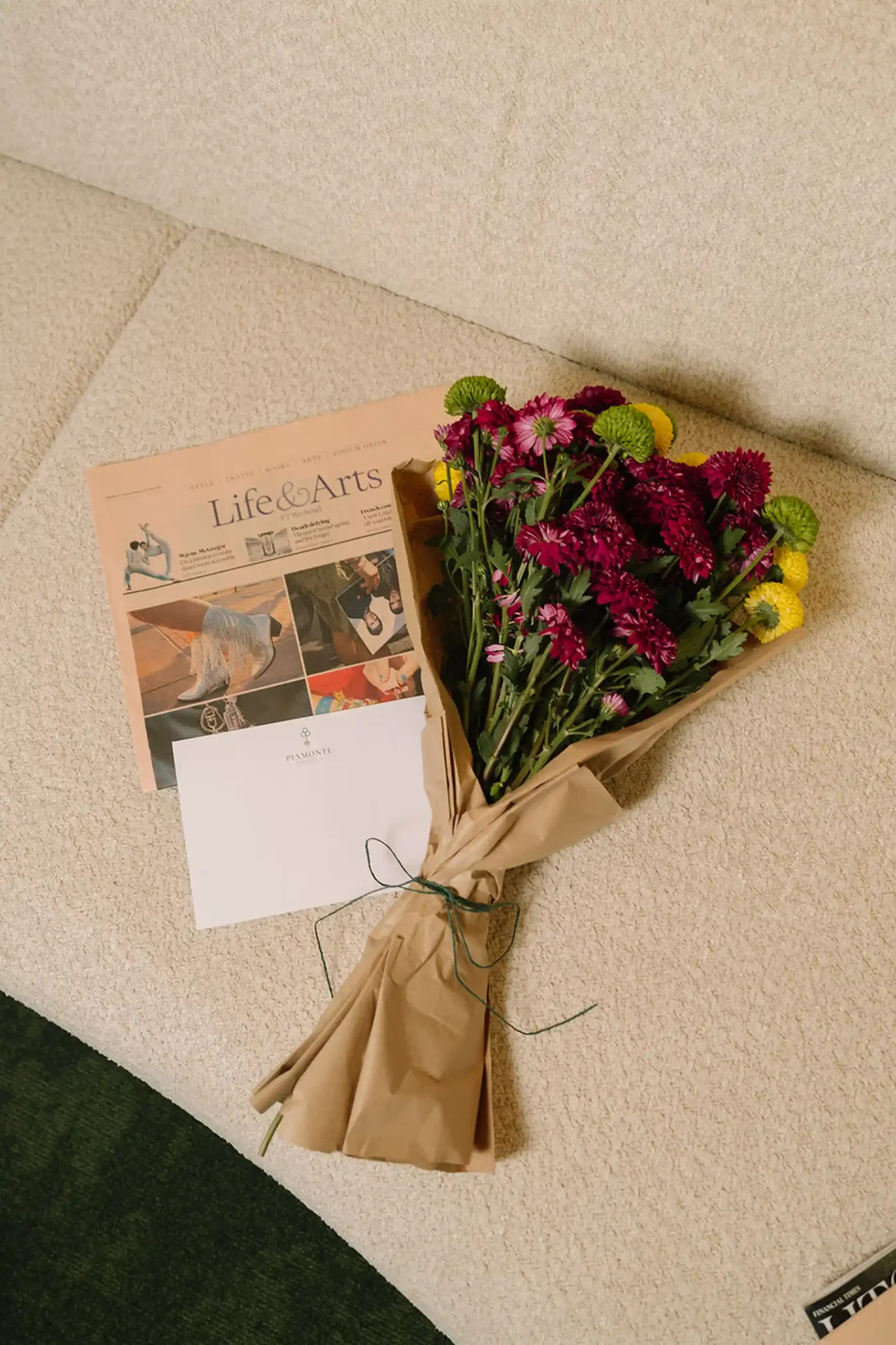 Bouquet de flores roxas e amarelas com um jornal em um sof&aacute; bege.