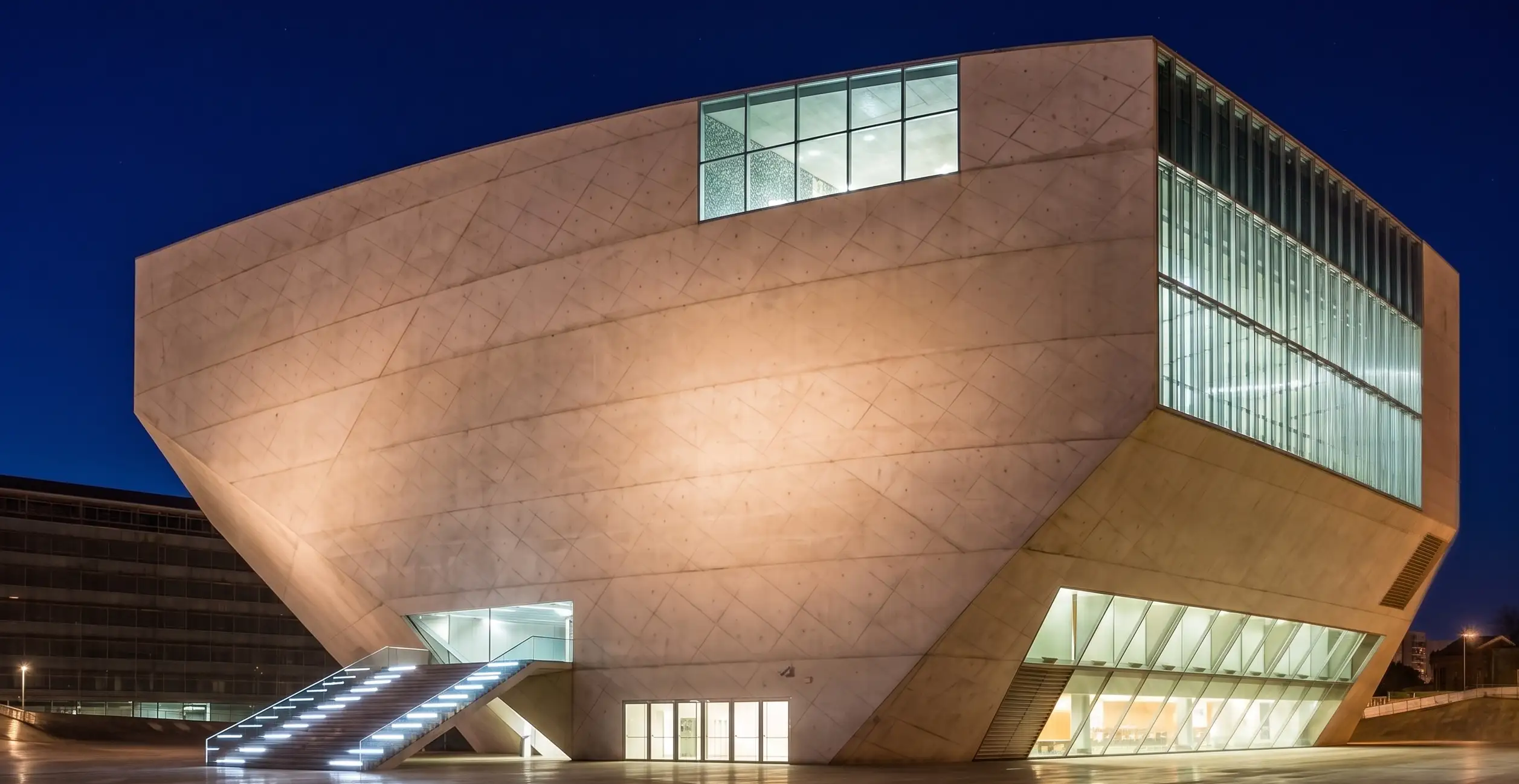 Edif&iacute;cio moderno iluminado &agrave; noite com janelas de vidro e degraus.