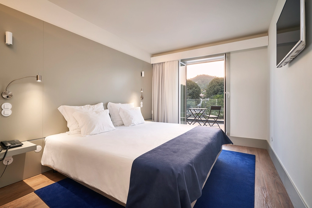 Quarto de hotel moderno com cama grande e varanda com vista.