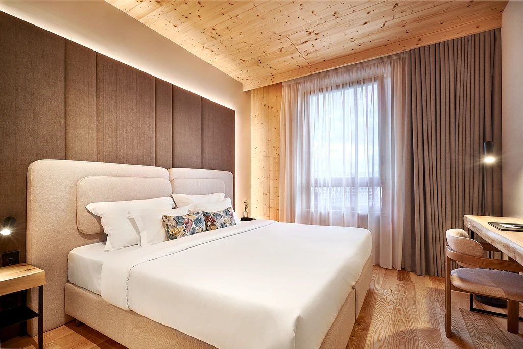 Quarto de hotel moderno com cama grande, cortinas e mesa de madeira.