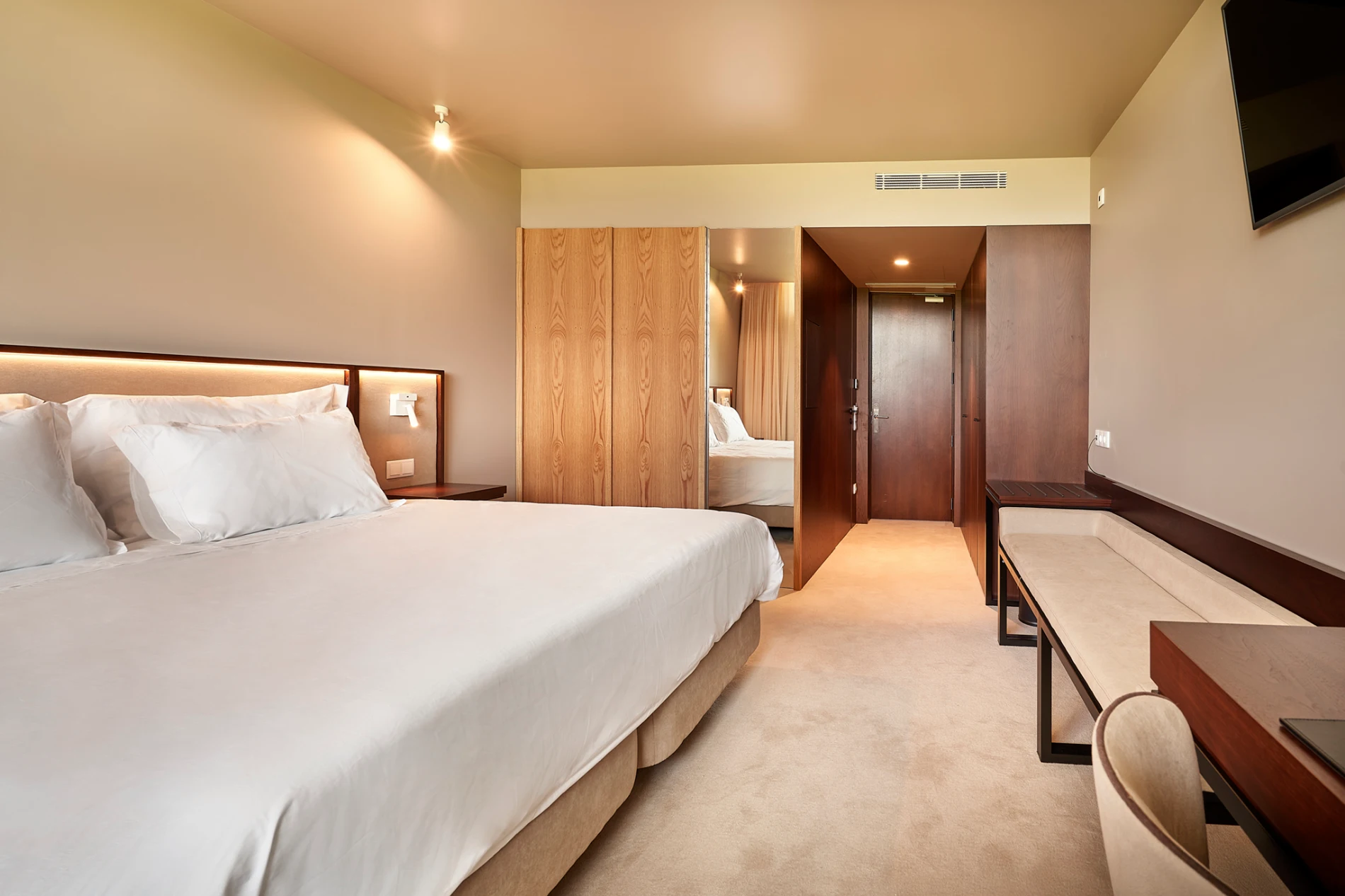 Quarto de hotel moderno com cama, poltrona e arm&aacute;rios de madeira, luz embutida