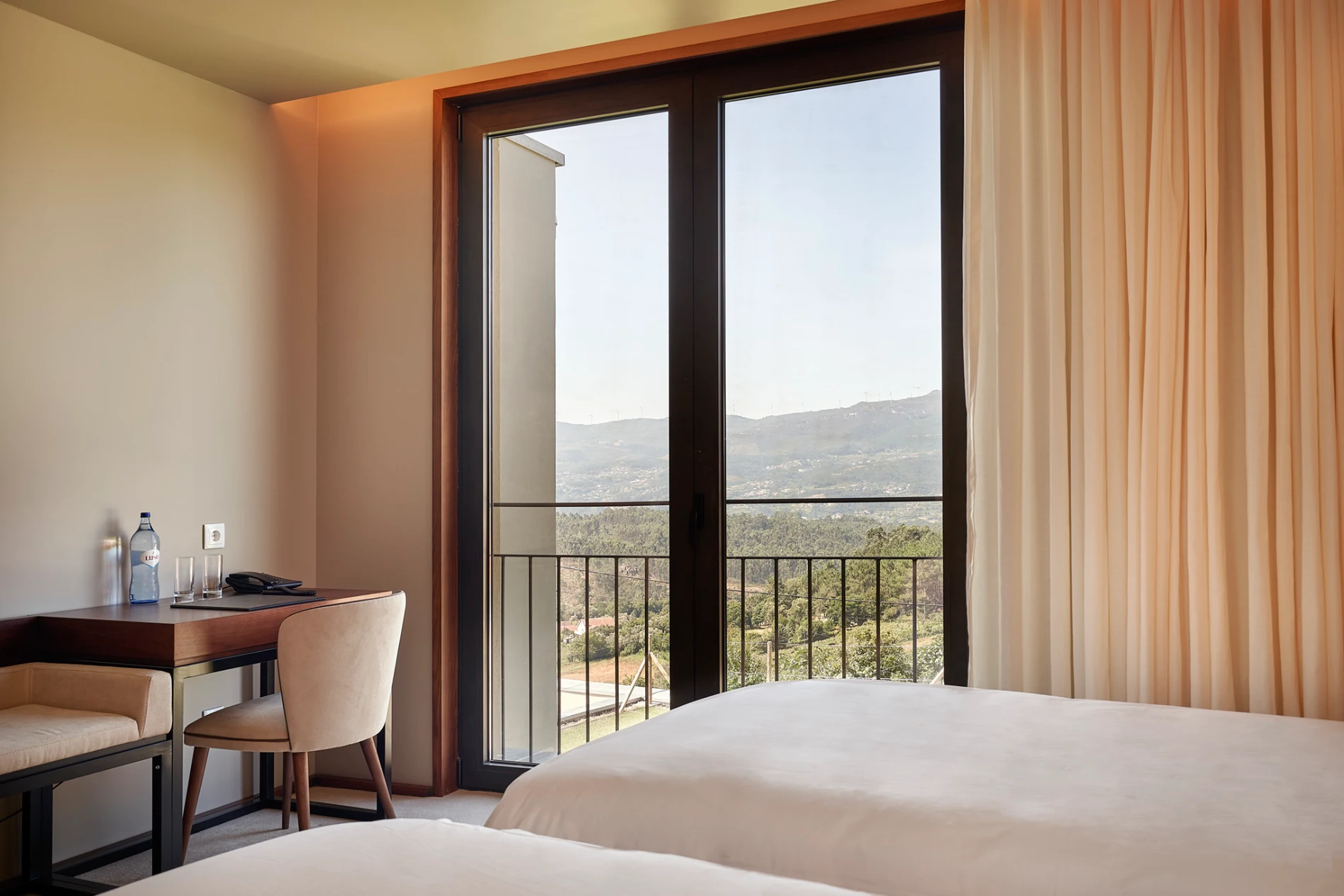 Quarto moderno com cama, mesa e portas de vidro com vista para montanhas