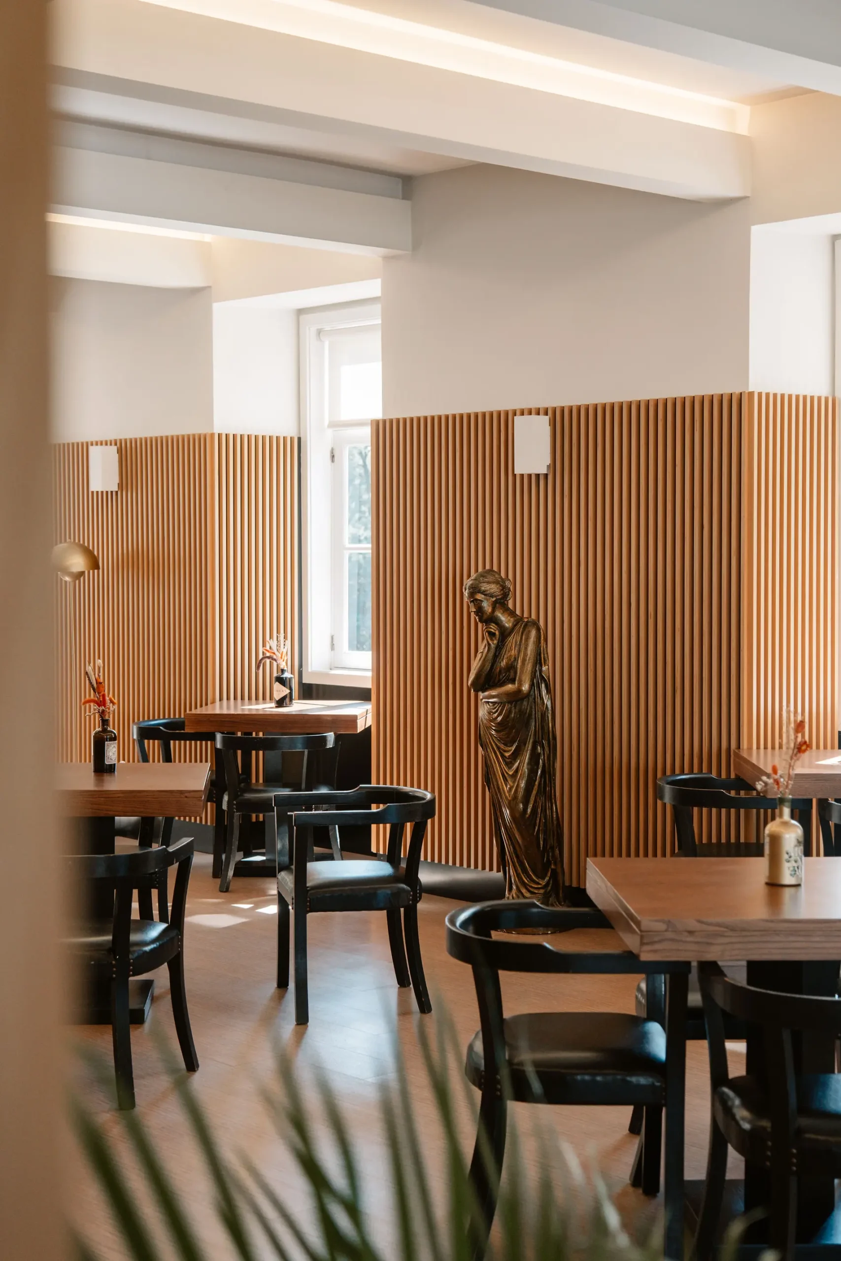 Sala de jantar moderna com mesas de madeira e est&aacute;tua cl&aacute;ssica.