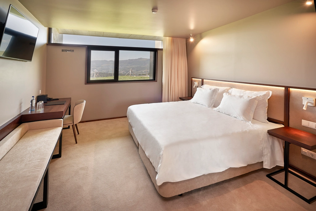 Quarto de hotel moderno com cama grande e vista para o exterior pela janela.