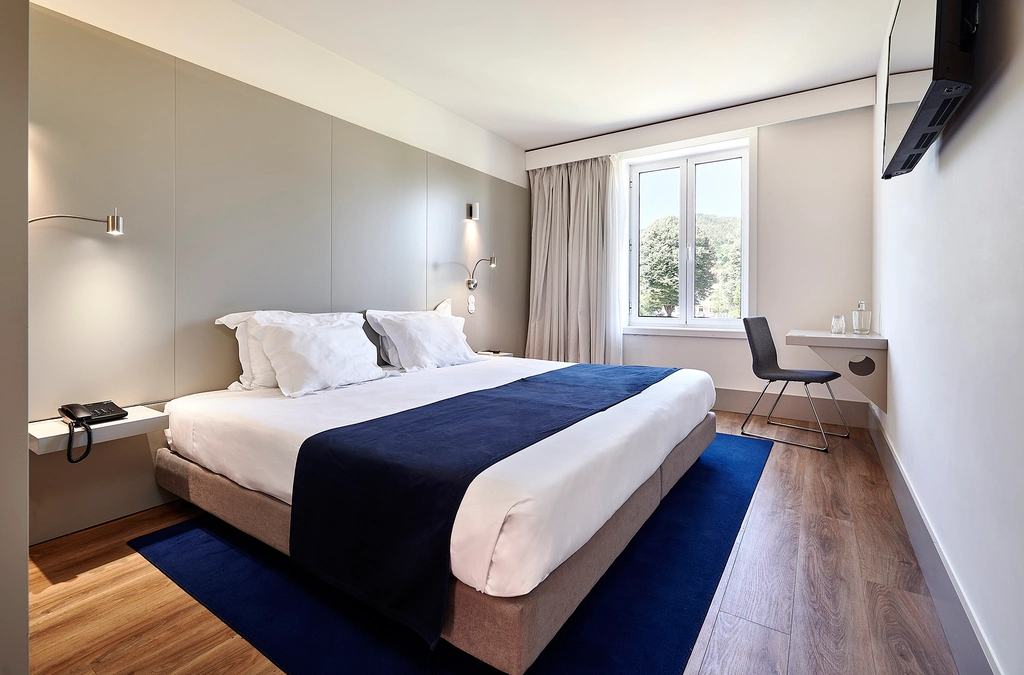 Quarto de hotel moderno com cama, mesa, cadeira e janela.