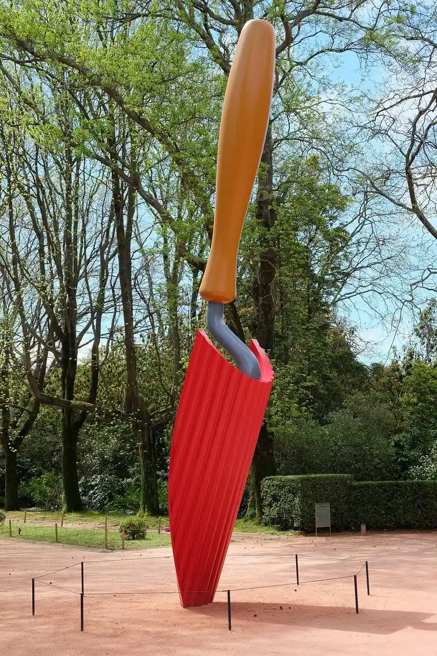 Escultura gigante de p&aacute; de jardinagem vermelha em parque arborizado.