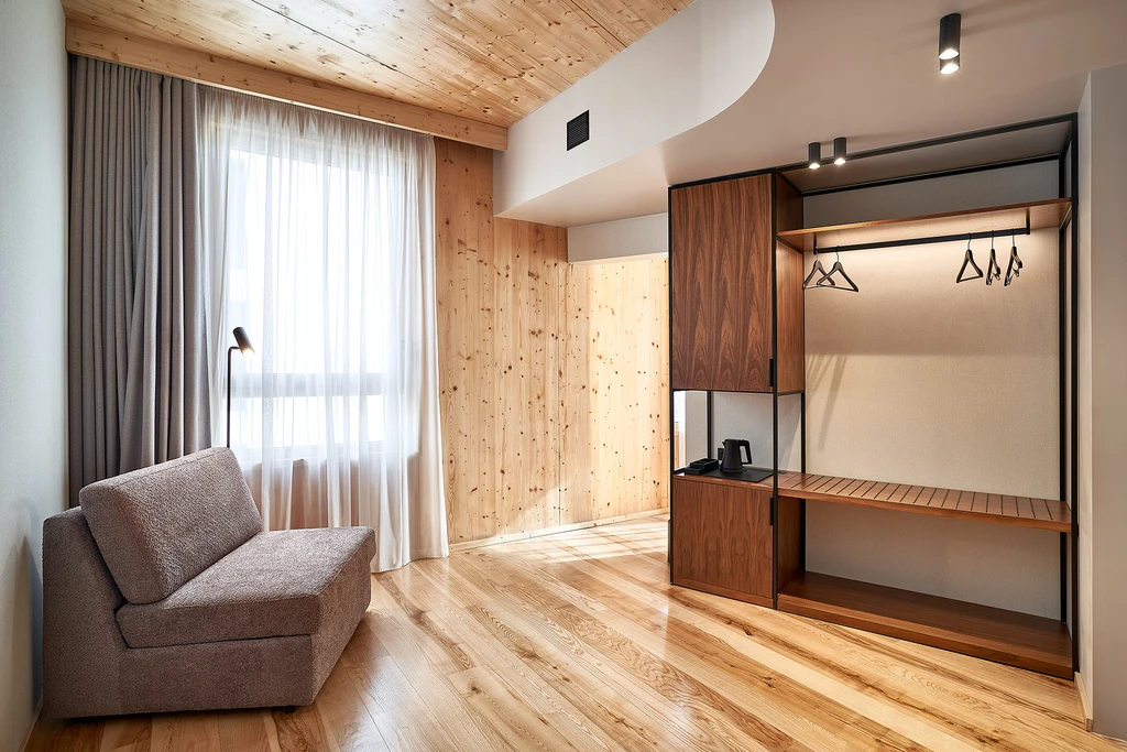 Quarto moderno com sof&aacute;, cortina e arm&aacute;rio de madeira iluminado.