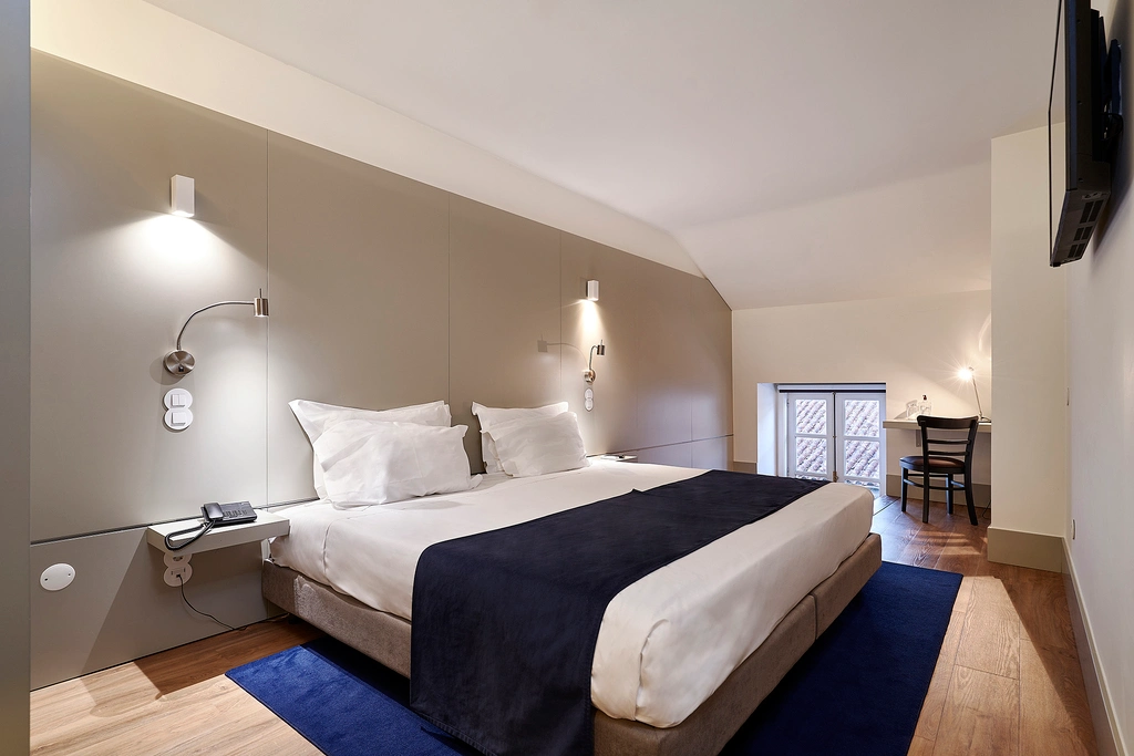 Quarto de hotel moderno com cama de casal e mesa, decora&ccedil;&atilde;o minimalista.