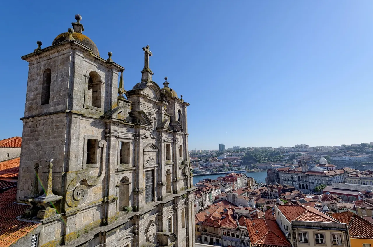 Edif&iacute;cio hist&oacute;rico com vista para cidade e rio, c&eacute;u azul ao fundo.
