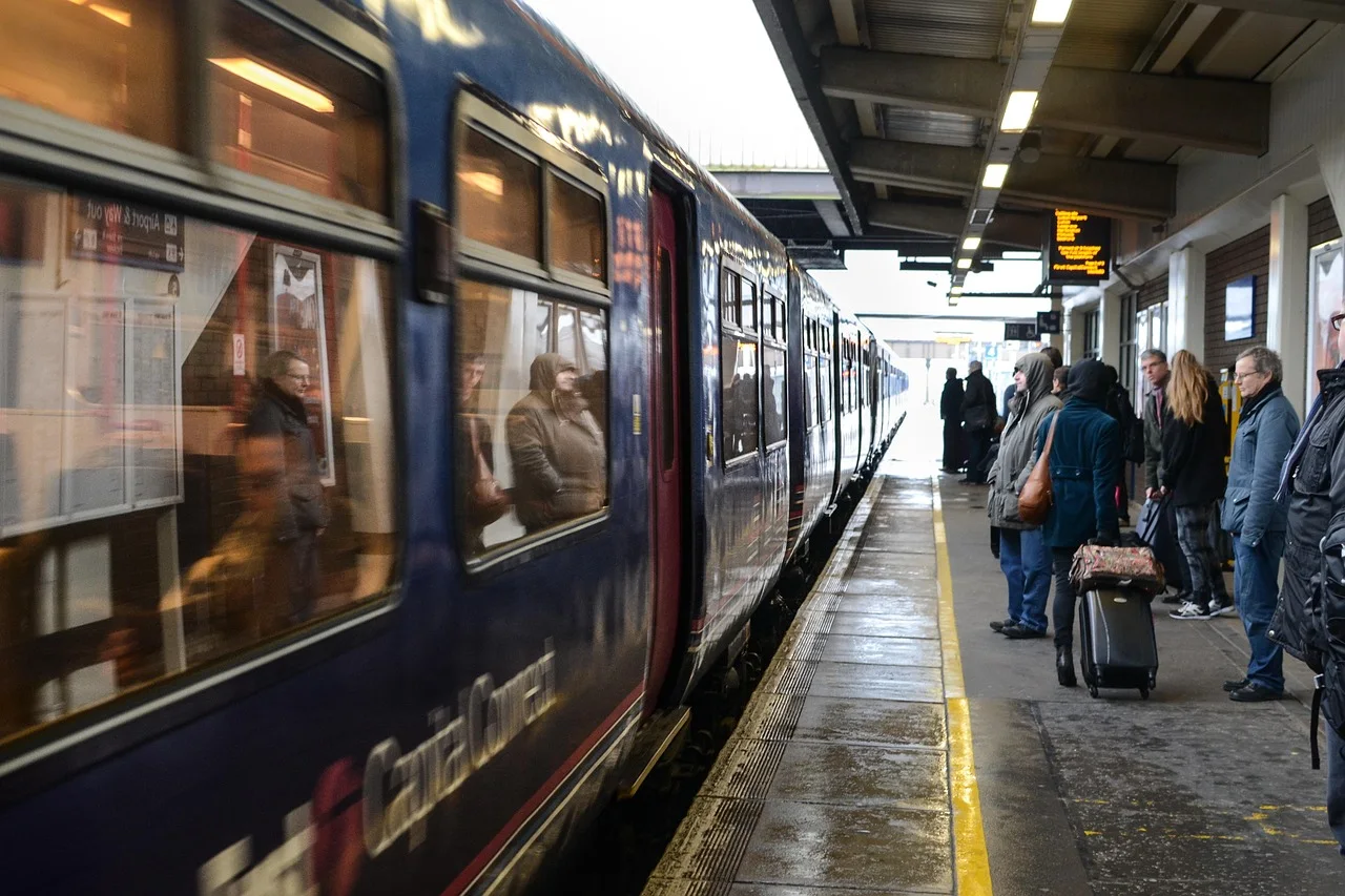 Trem parado em esta&ccedil;&atilde;o, passageiros aguardando na plataforma.