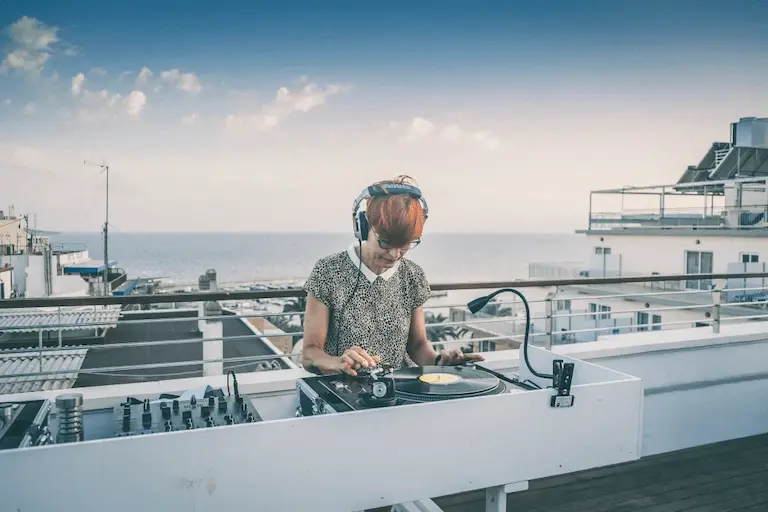 DJ con aud&iacute;fonos y consola en la azotea frente al mar, cielo nublado