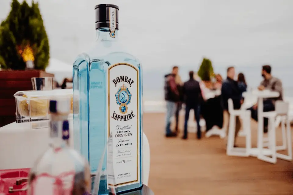Botella Bombay Sapphire en evento al aire libre, fondo con personas y mesa