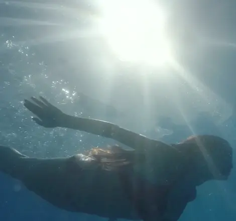 Tibur&oacute;n nadando bajo el agua, con luz solar y manos en la superficie