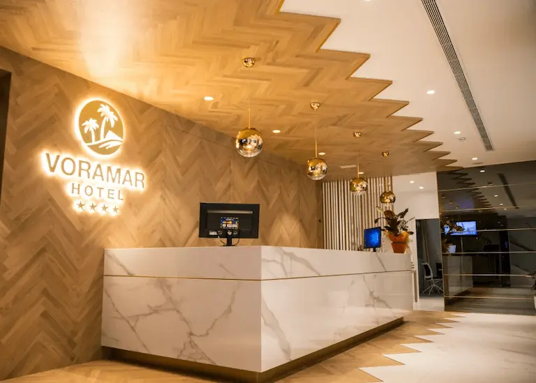 Recepci&oacute;n del Hotel Voramar con mostrador y logotipo luminoso.