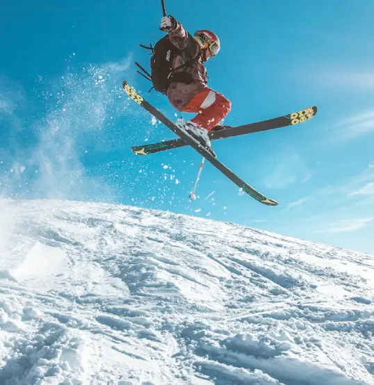 Esquiador haciendo un salto sobre la nieve, con el cielo azul de fondo