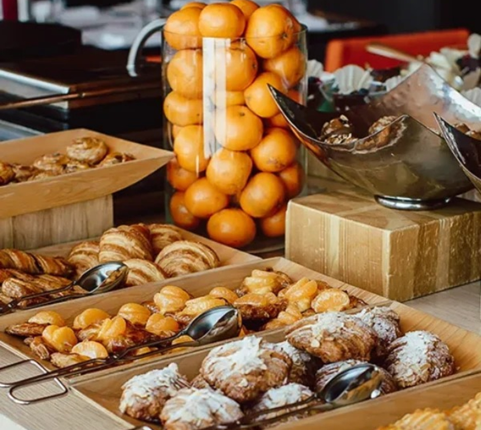 Bandejas con panes y bollos, y una pila de naranjas en el mostrador buffet