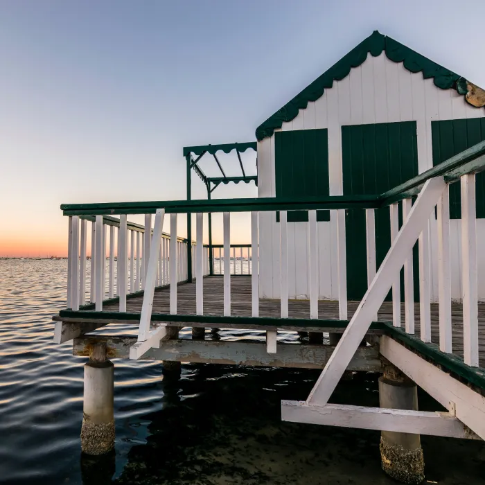 Casa sobre el agua al atardecer, con barandilla verde y blanca.