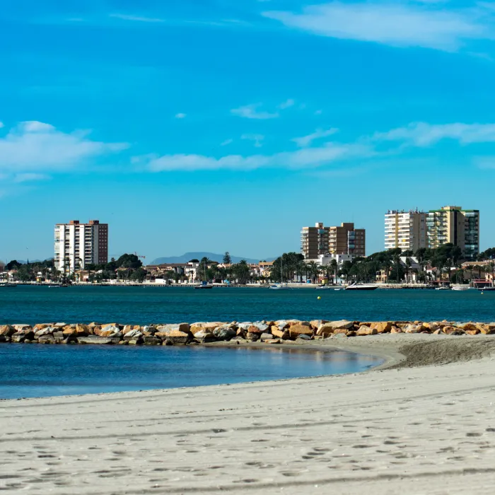 Playa con edificios al fondo y cielo azul.