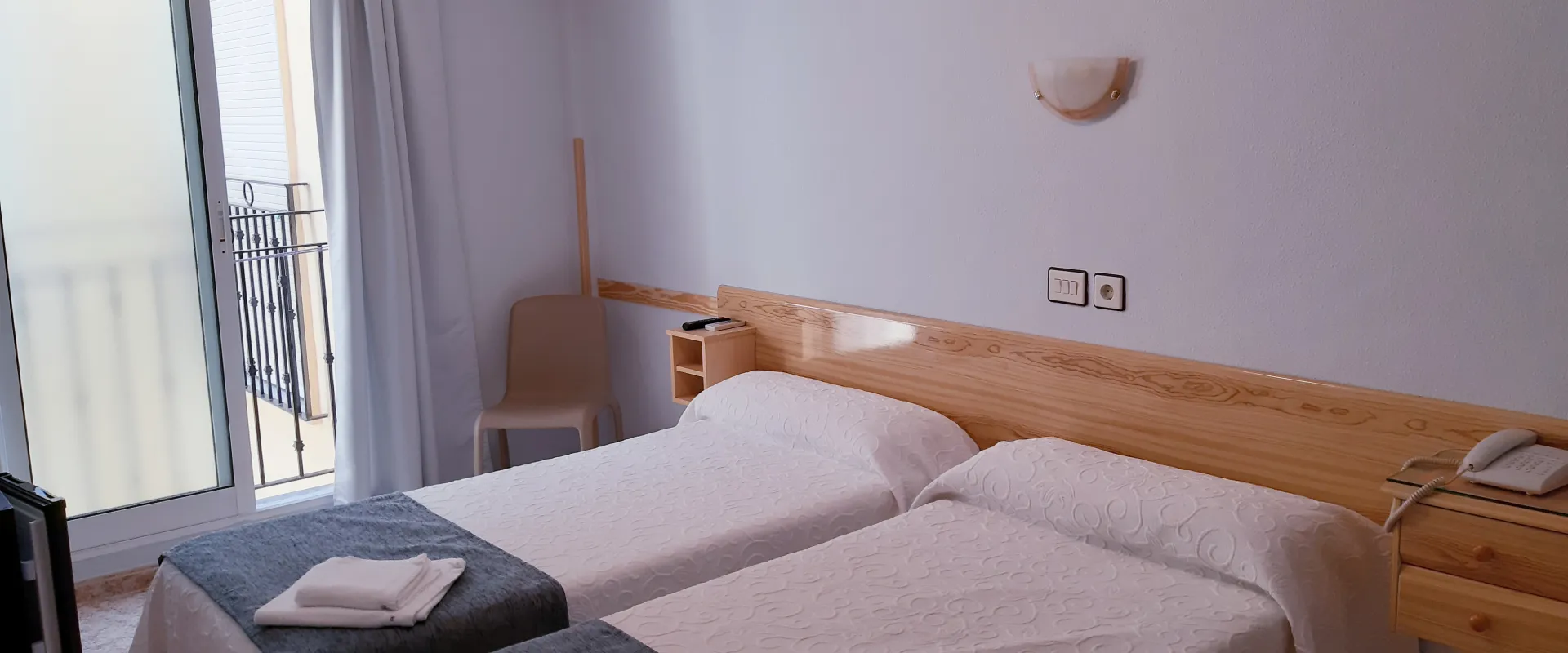 Habitaci&oacute;n de hotel con dos camas individuales y luz natural.