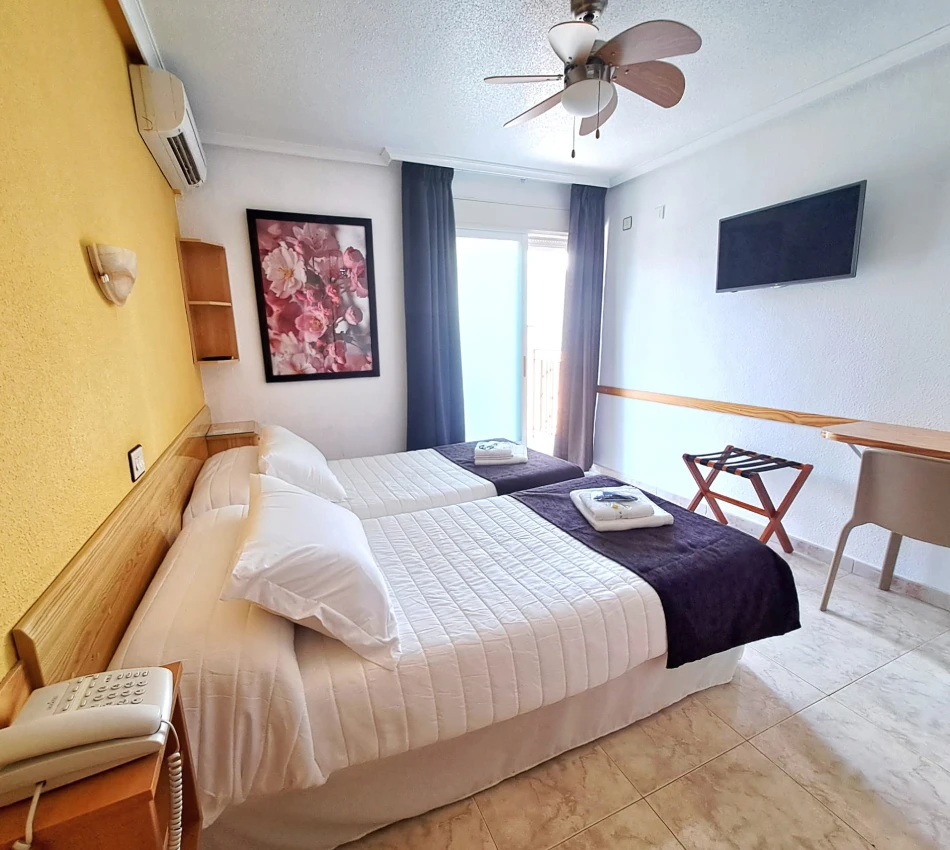 Habitaci&oacute;n doble con dos camas, cortinas azules y ventilador de techo
