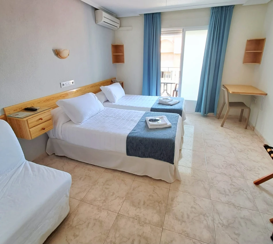 Habitaci&oacute;n doble con camas blancas, cortinas azules y escritorio de madera.