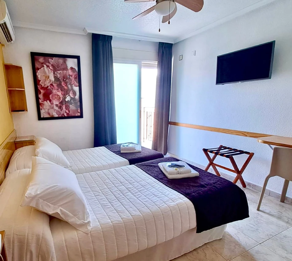 Dormitorio con cama doble, mesitas, cortinas azules y televisor en pared