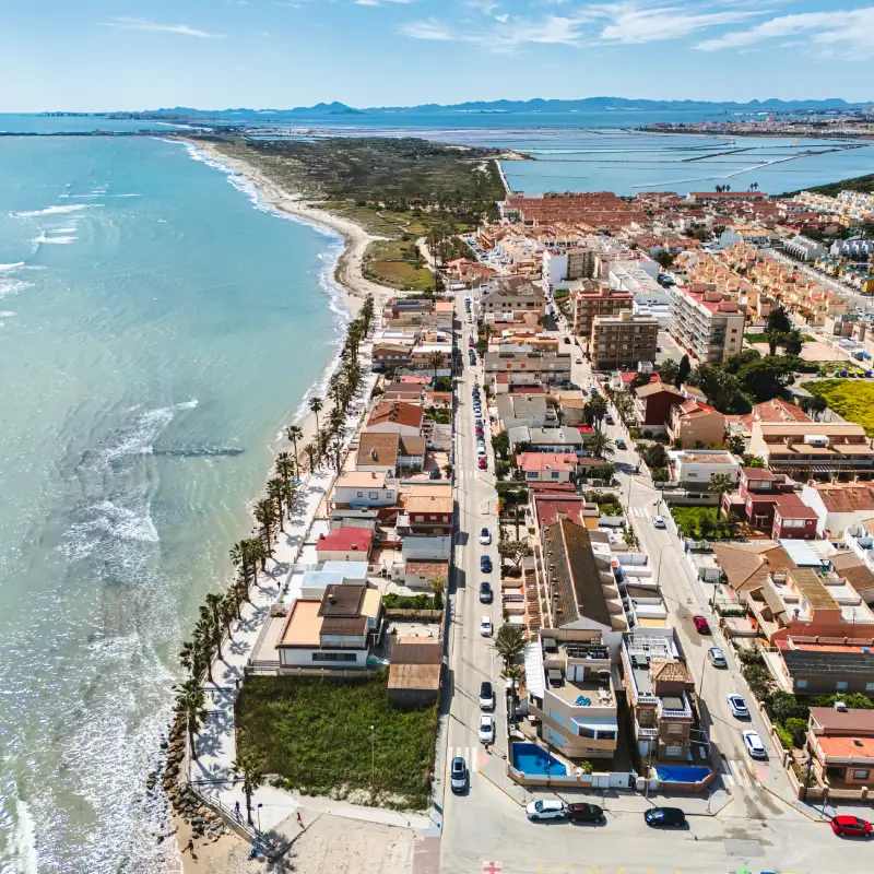 Vista a&eacute;rea de un pueblo costero con playa y edificios alineados junto al mar.