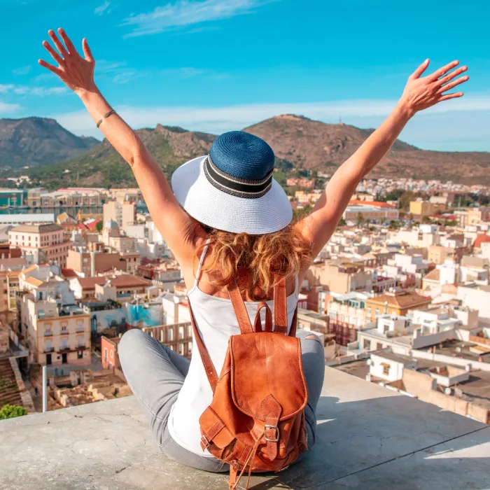 Mujer sentada con los brazos levantados, disfrutando de una vista urbana y monta&ntilde;as.