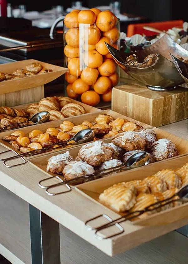 Bandejas con panes y bollos, y una pila de naranjas en el mostrador buffet
